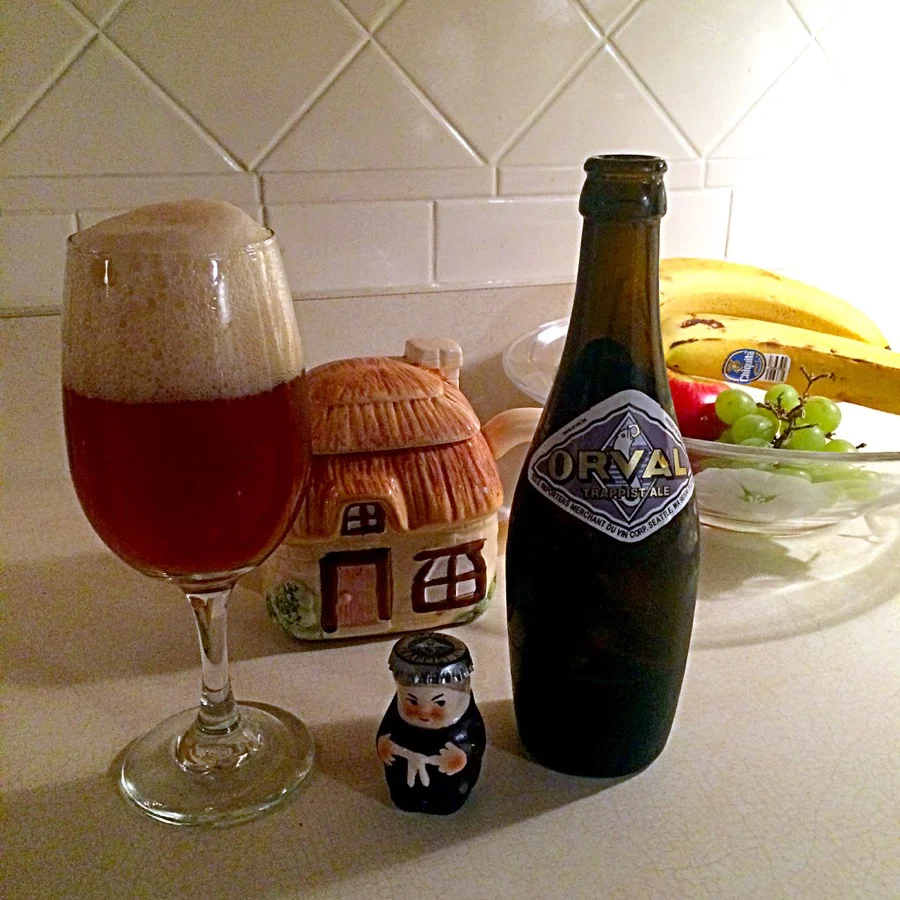 Verre d'Orval à la robe cuivrée coiffée d'une mousse dense, à côté de sa bouteille